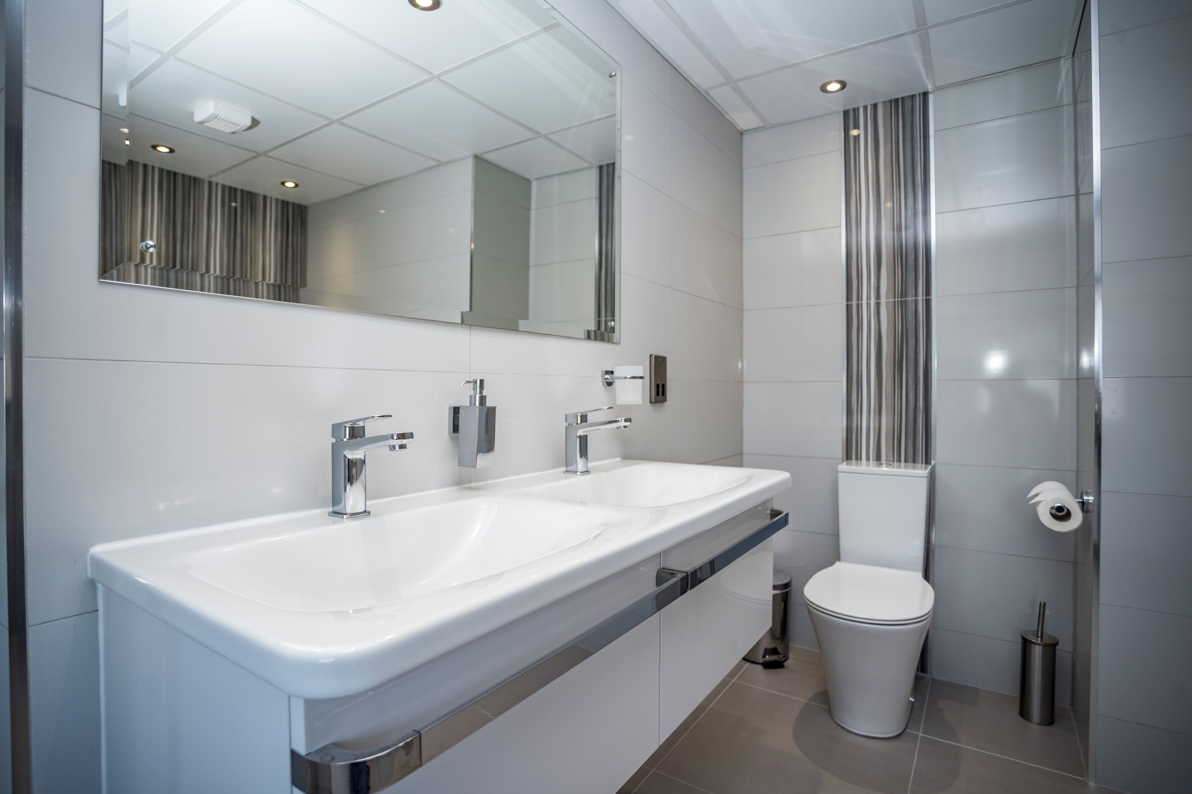 A modern bathroom with two sinks, a toilet, and a mirror.