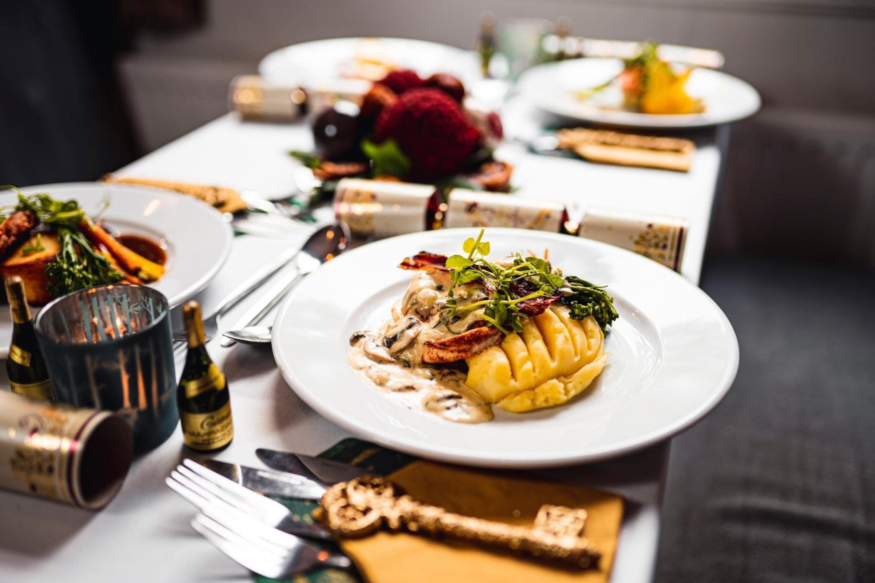 A dining table set with plates of food, wine bottles, and cutlery.