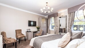 A bedroom with a bed, two armchairs, a desk, a television, and a large mirror. - Borough Arms Hotel (Newcastle-Under-Lyme)