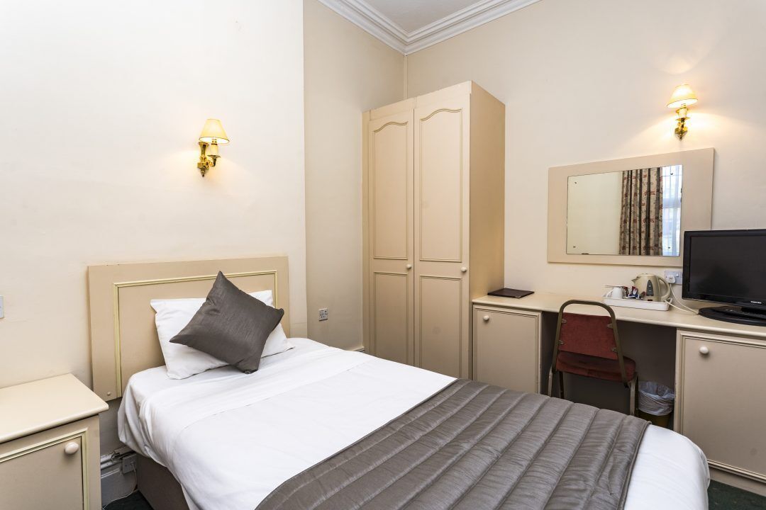 A hotel room with a bed, a desk with a chair, a wardrobe, and a television.