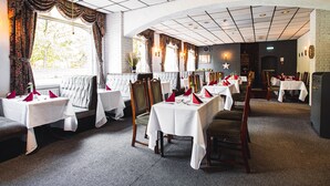 A restaurant with multiple tables set for dining, featuring white tablecloths and red napkins. - Borough Arms Hotel (Newcastle-Under-Lyme)