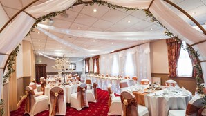 A banquet hall with round tables, white tablecloths, and chairs with gold sashes. - Borough Arms Hotel (Newcastle-Under-Lyme)
