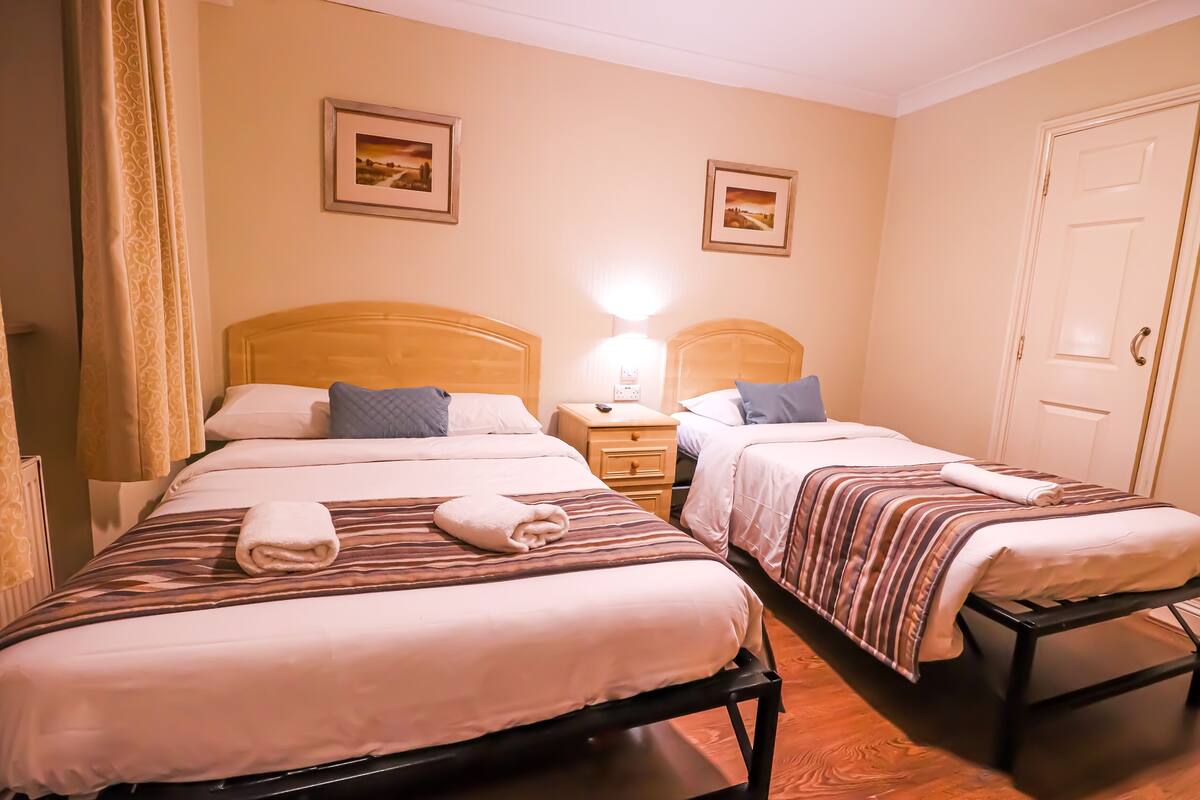 A hotel room with two beds, each with a wooden headboard, a bedside table with a lamp, and a door.