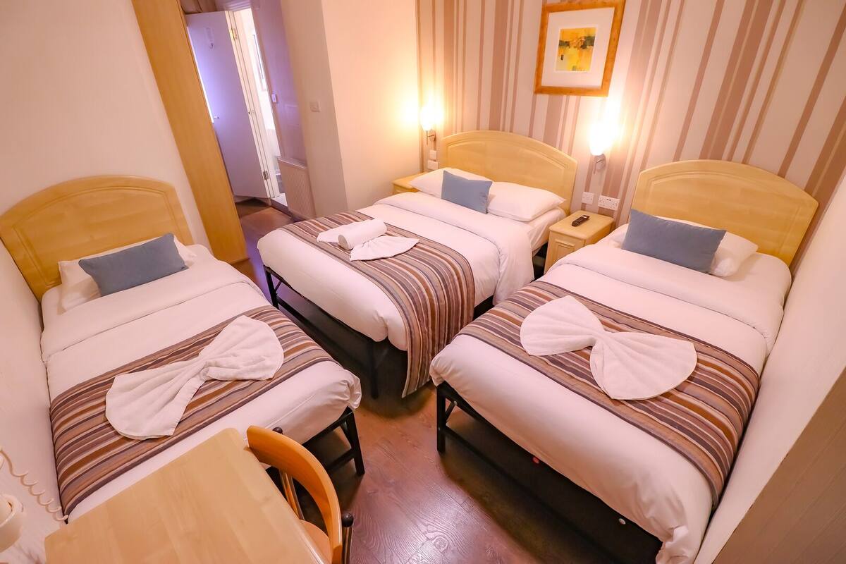 A hotel room with three beds, each with striped bedding and towels. There is a wooden chair and a small table.