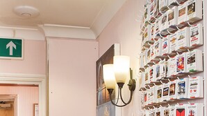 A hotel reception area with a wooden reception desk, a wall-mounted display of magazines, and a fire extinguisher. - The Fairway Hotel (London)
