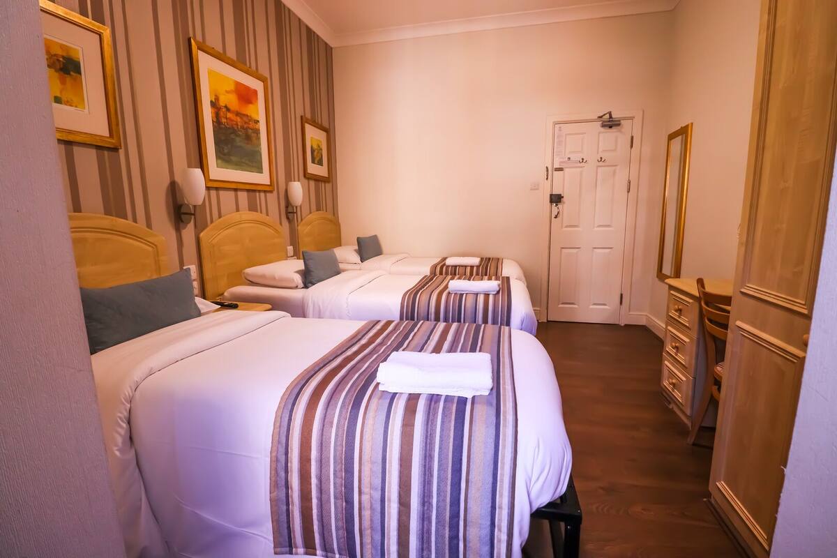 A hotel room with two beds, striped bedding, a wooden dresser, and a door with a mirror.