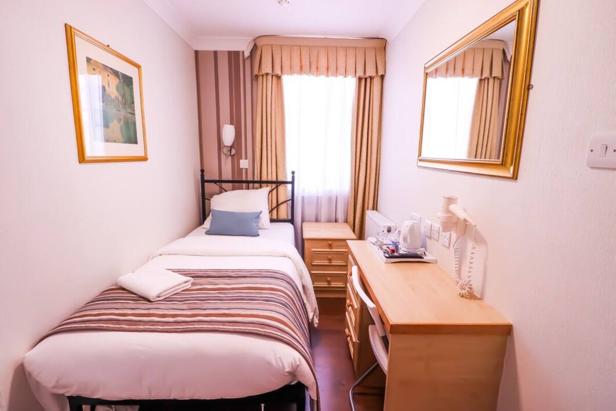 A hotel room with a bed, a desk, a chair, a telephone, and a mirror.