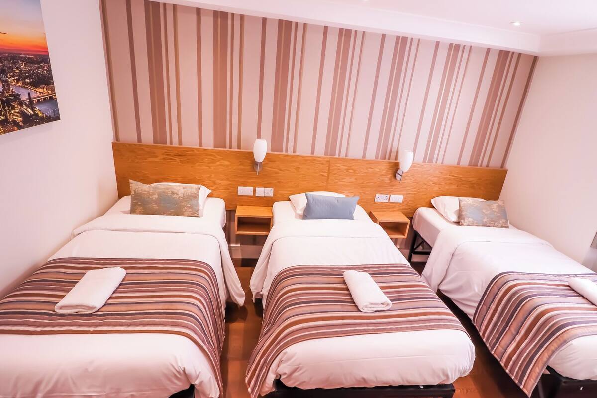 A hotel room with three single beds, wooden headboards, and a cityscape view.