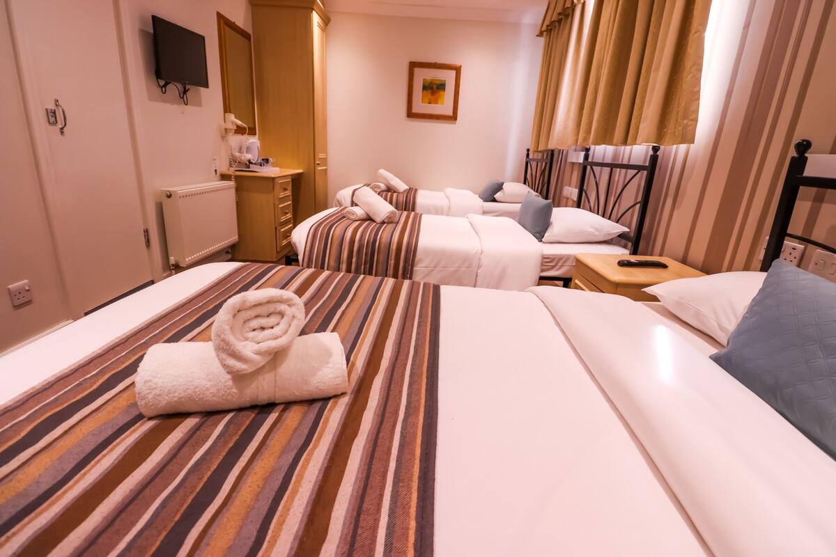A hotel room with two beds, a TV, a painting, and a window with curtains.