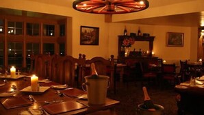 A warmly lit dining room with a chandelier, wooden furniture, and a table set for a meal. - Chequers Inn Hotel (Forest Row)