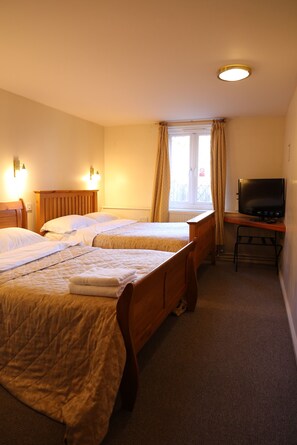 A hotel room with two beds, a desk with a television, and a window with curtains.