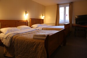 A hotel room with two single beds, a wooden headboard, a desk with a television, and a window with curtains.