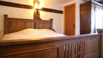 A wooden bed with a headboard, a wall-mounted light fixture, and a door in the background.
