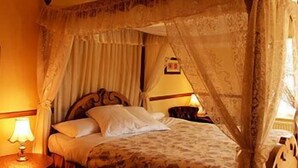 A four-poster bed with a canopy, a bedside table with a lamp, and a chair in a warmly lit room. - Chequers Inn Hotel (Forest Row)