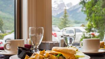 A meal with a sandwich and potatoes, two cups, and a glass on a table with a mountain view in the background.