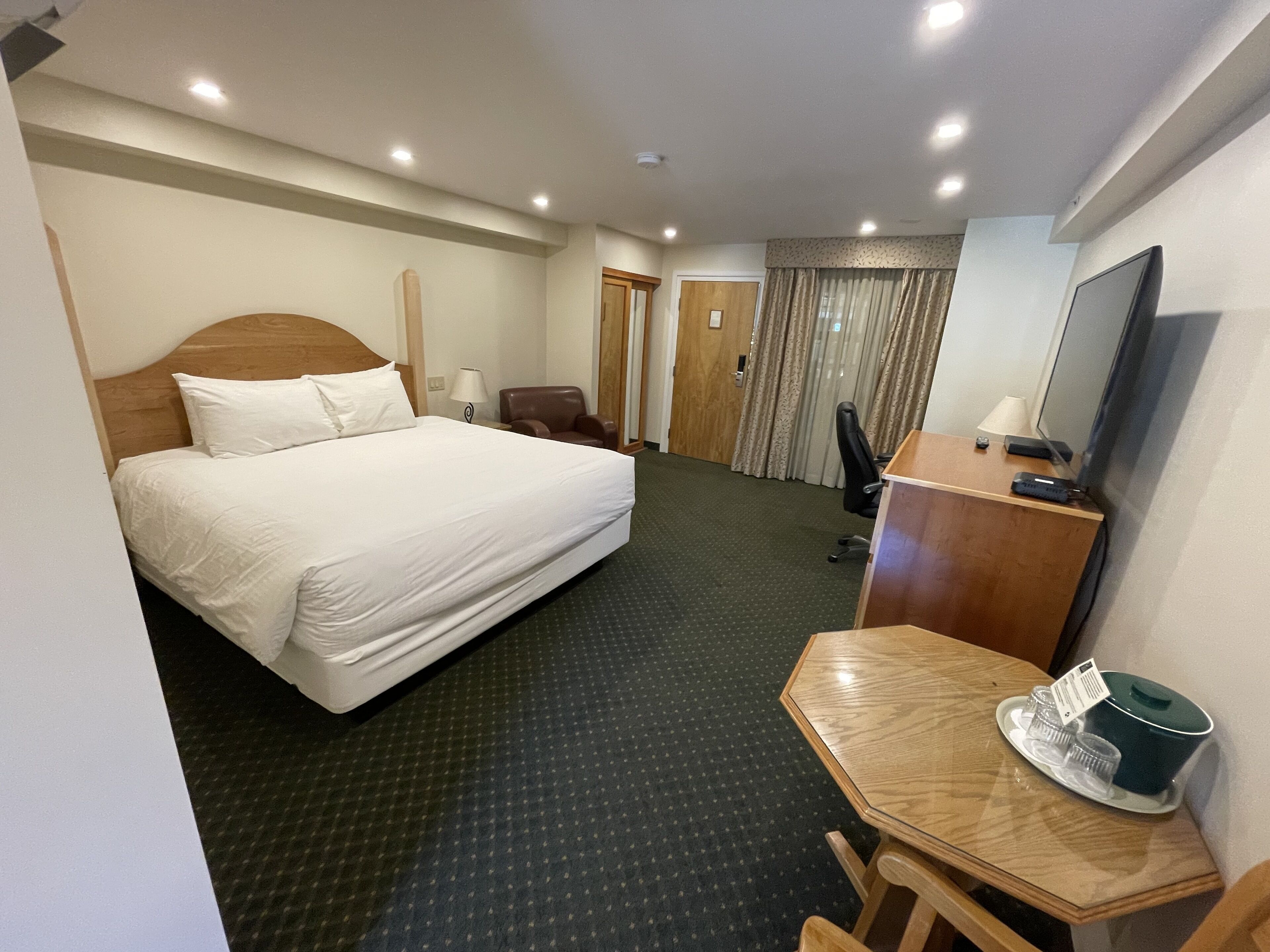 Una habitación de hotel con una cama grande, un escritorio con ordenador, una silla, un televisor y una pequeña mesa con tetera y tazas.