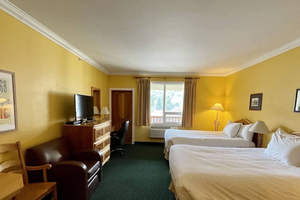 Una habitación de hotel con escritorio, dos camas, televisión y ventana con cortinas.