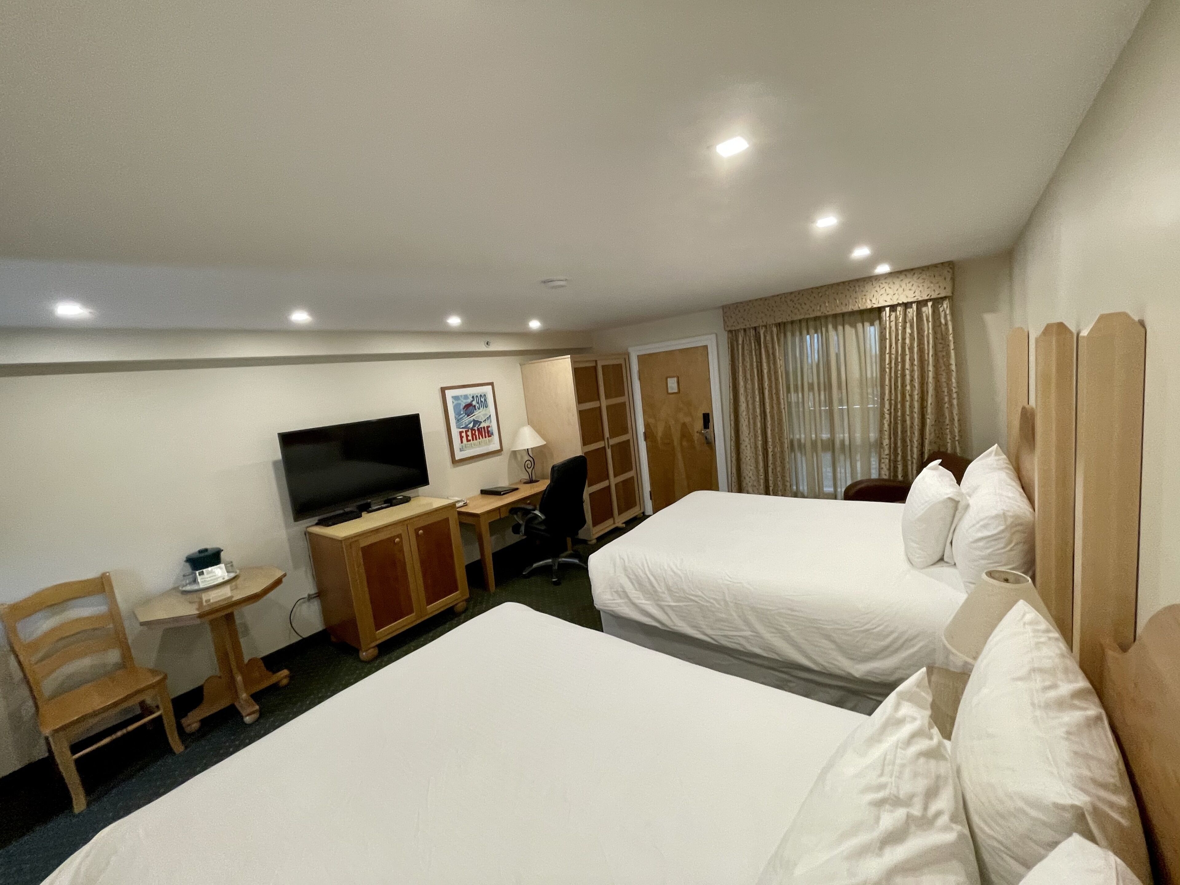 A hotel room with two beds, a desk with a television, a chair, and a small table.