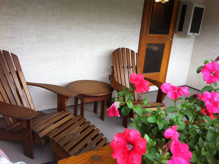 Een houten stoel en tafel staan voor een structuurwand, met een deur en een airconditioner op de achtergrond.