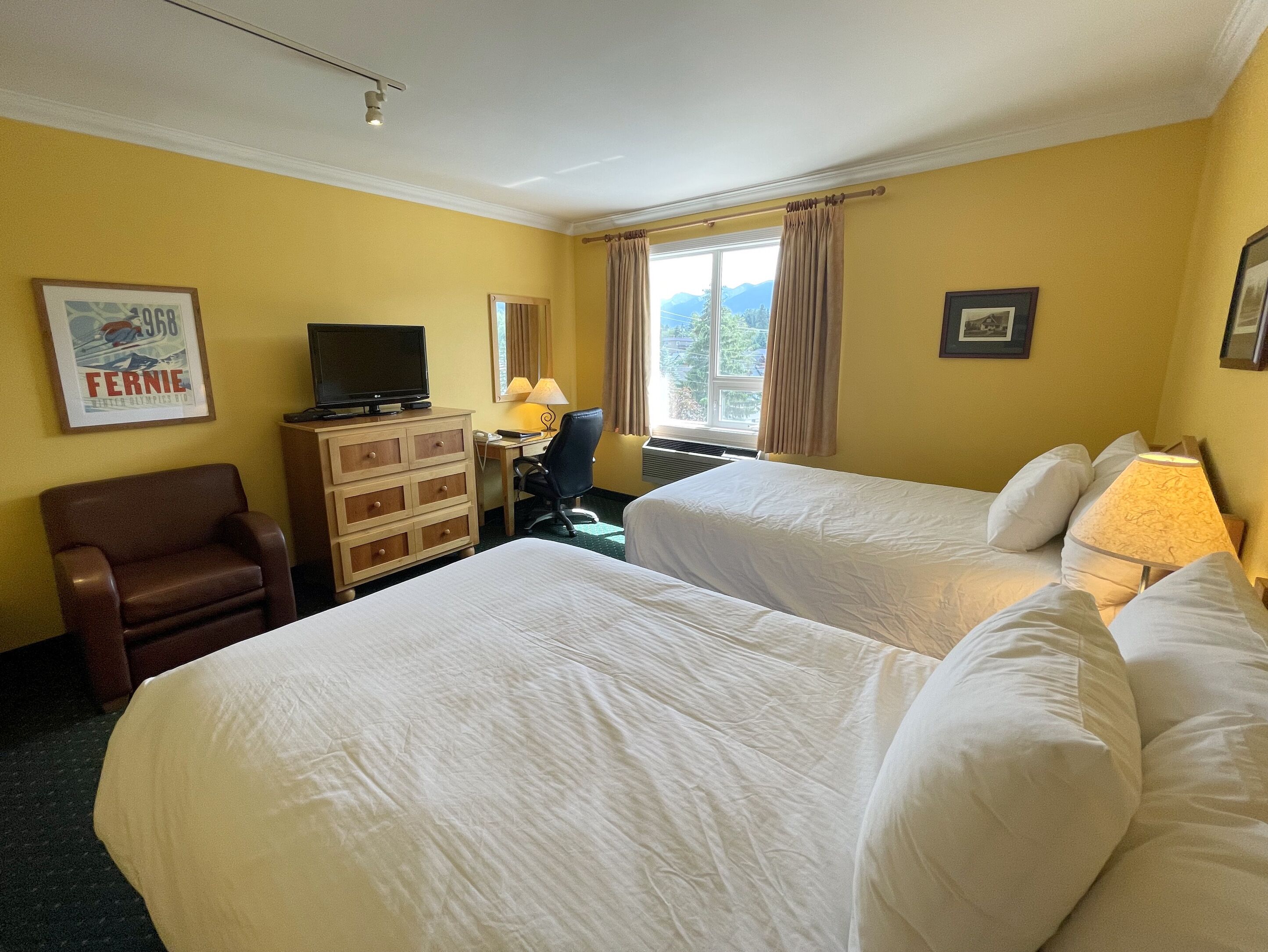 A hotel room with two beds, a desk with a chair, a television, and a dresser.