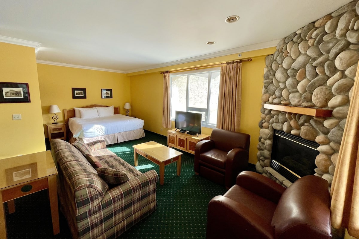 Habitación de hotel con cama, televisión, chimenea, sofá, sillón y una mesita.