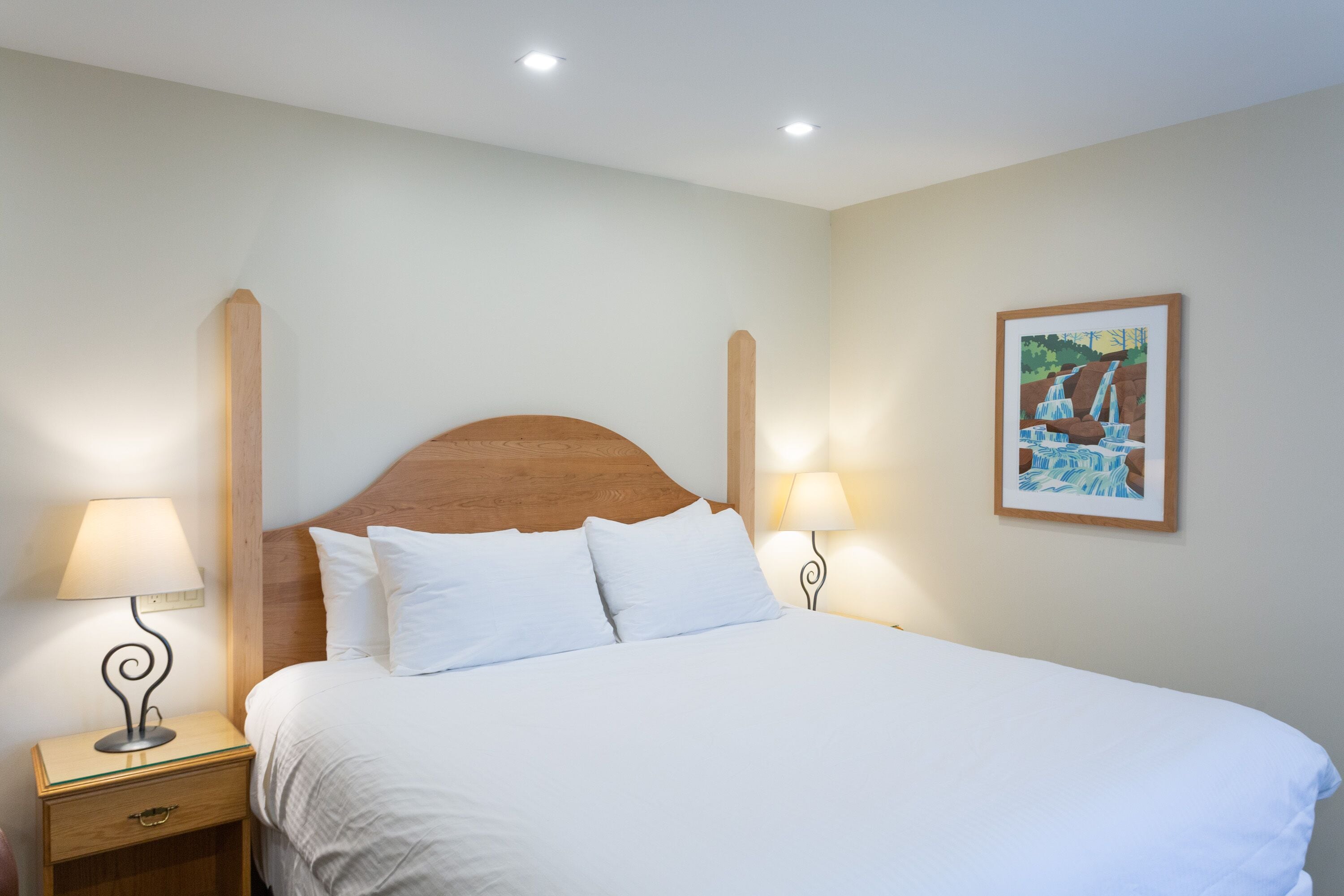 A neatly made bed with white linens, two bedside tables with lamps, and a framed picture on the wall.