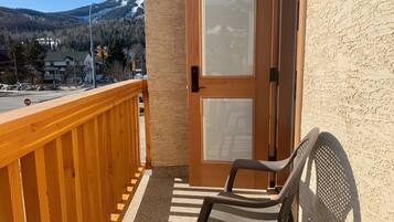 A balcony with a wooden railing, a chair, and a door with two windows.