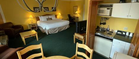 A hotel room with a bed, a TV, a dining table, and a kitchenette.