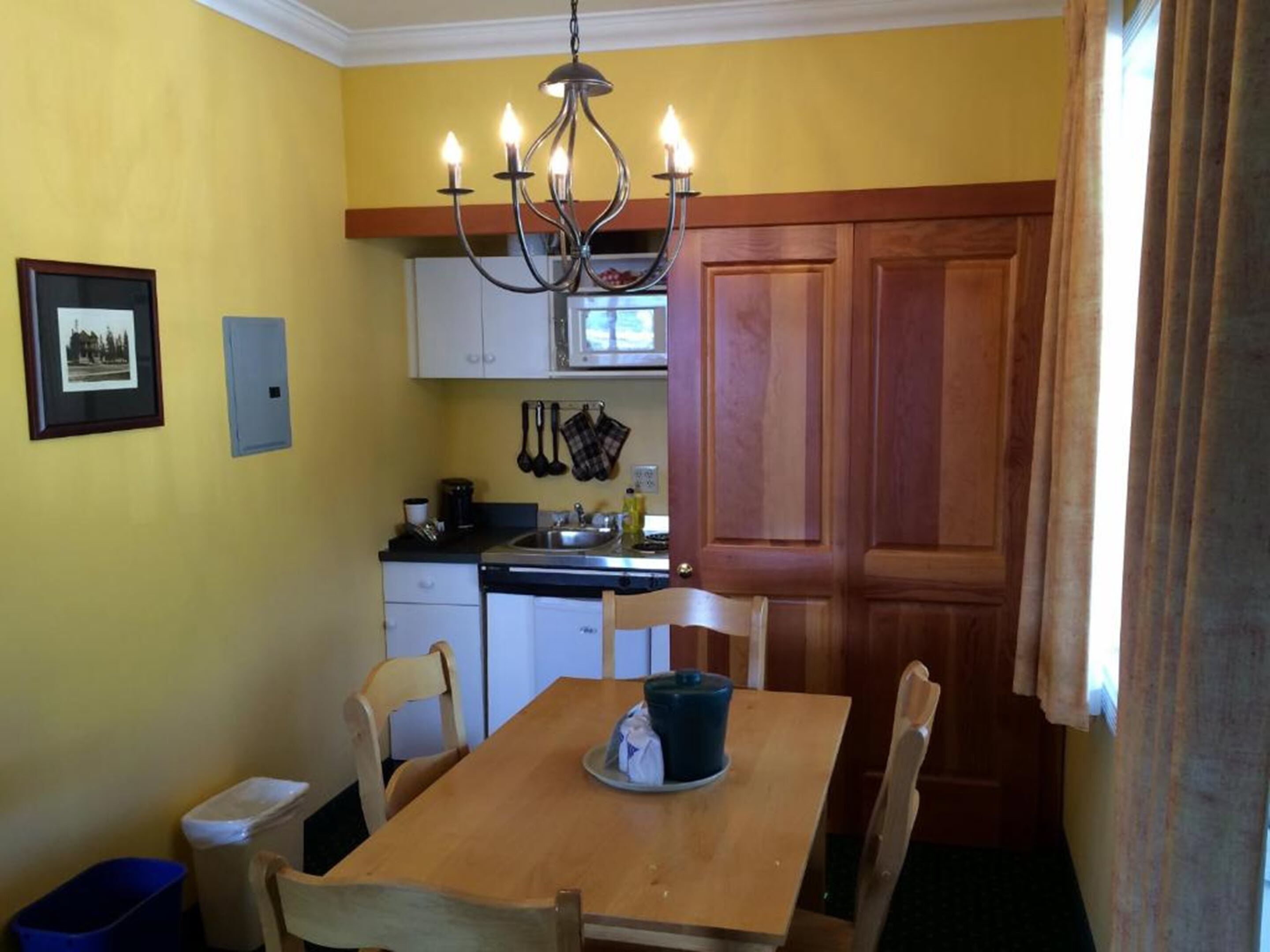 A compact kitchen with a dining table, chairs, a chandelier, and a wooden door.