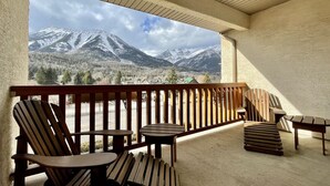 A balcony with wooden chairs and tables, offering a view of snow-capped mountains and a forested valley. - Park Place Lodge (Fernie)