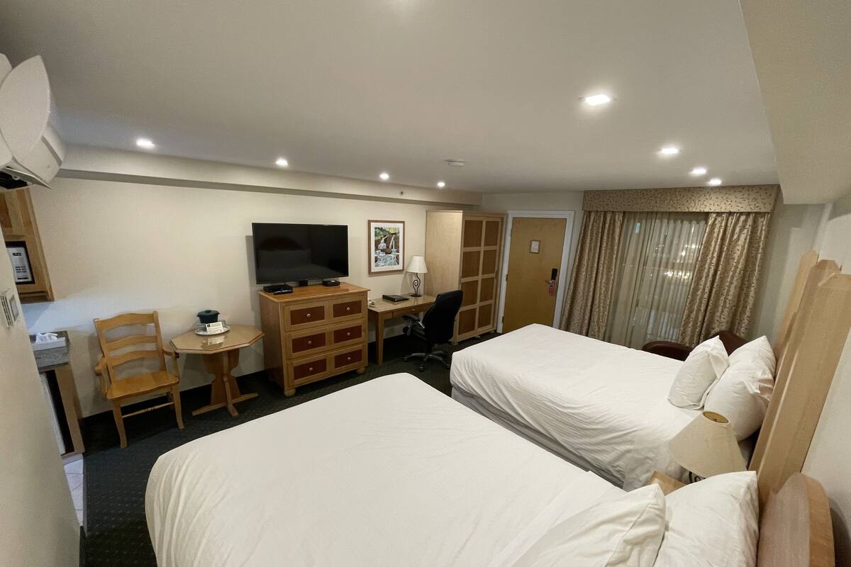 Una habitación de hotel con dos camas, un escritorio, un televisor y un armario.
