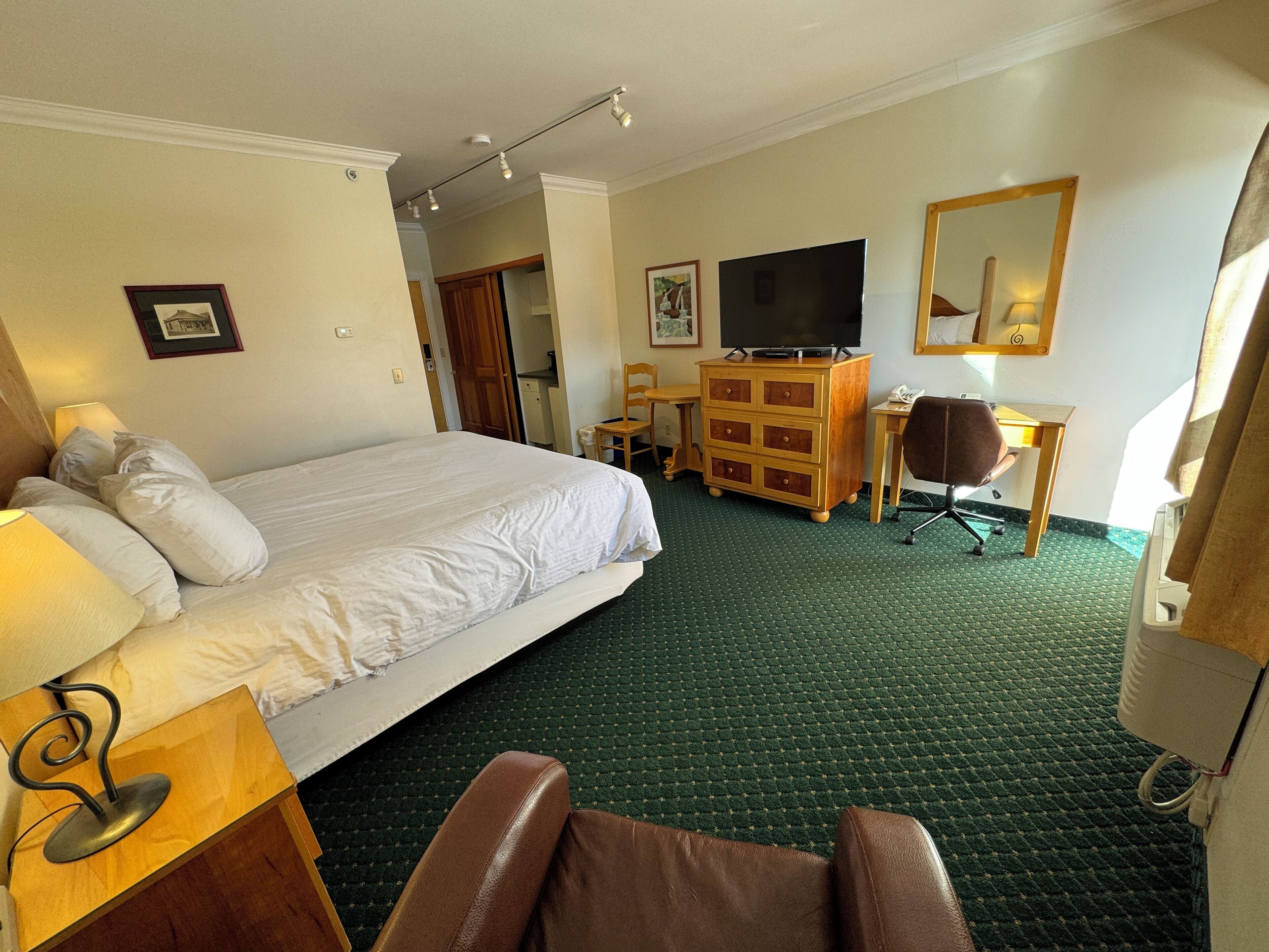 A hotel room with a bed, a desk, a chair, a dresser, a television, and a mirror.