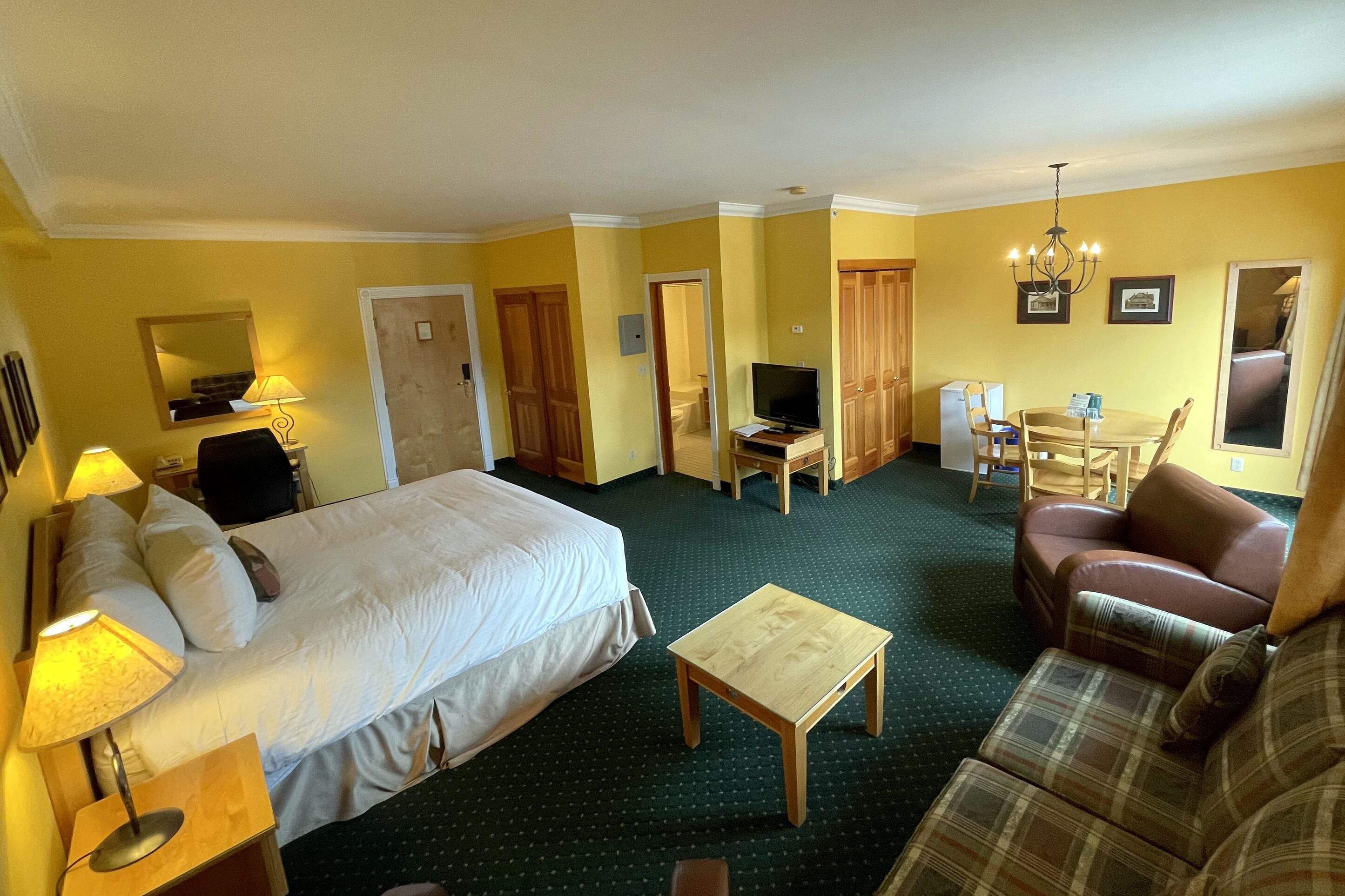 A hotel room with a bed, a small table, a sofa, a TV, and a dining area with chairs.