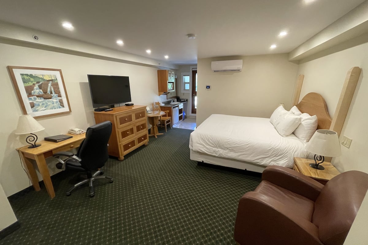 Habitación de hotel con cama, escritorio, silla, televisor, cómoda y aire acondicionado.