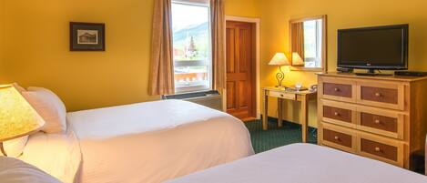 A hotel room with two beds, a desk with a lamp, a television, and a window with curtains.