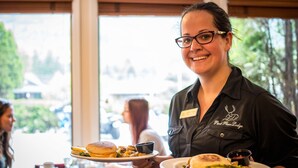 A person holding a plate with food, wearing a name tag, and a black shirt with a logo. - Park Place Lodge (Fernie)