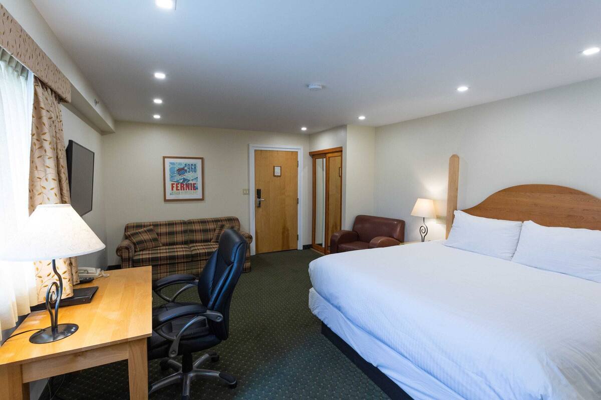 Habitación de hotel con cama, escritorio con lámpara, silla, sofá y televisor.