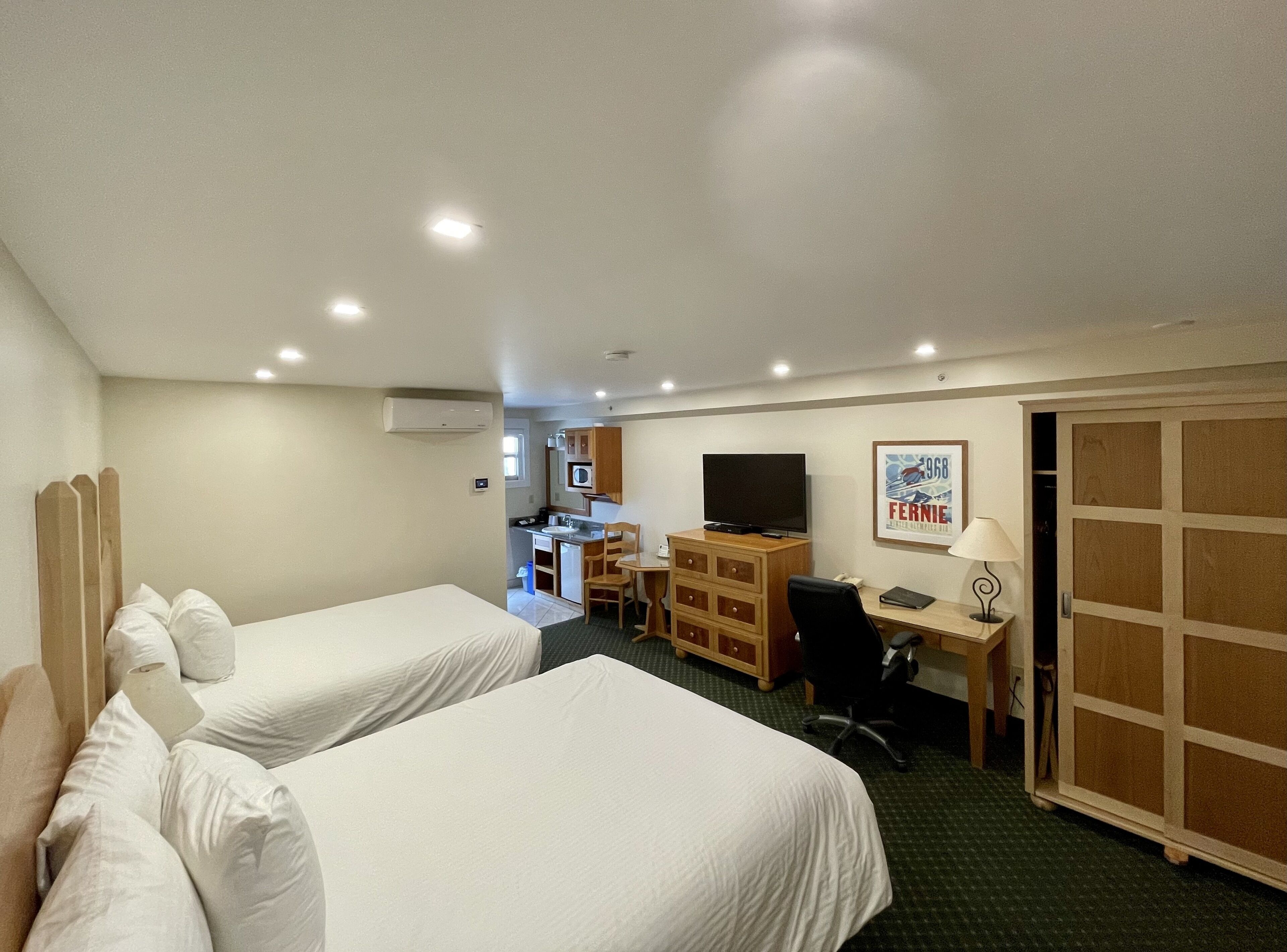 Une chambre d’hôtel avec deux lits, un bureau avec un ordinateur, une télévision et une armoire.