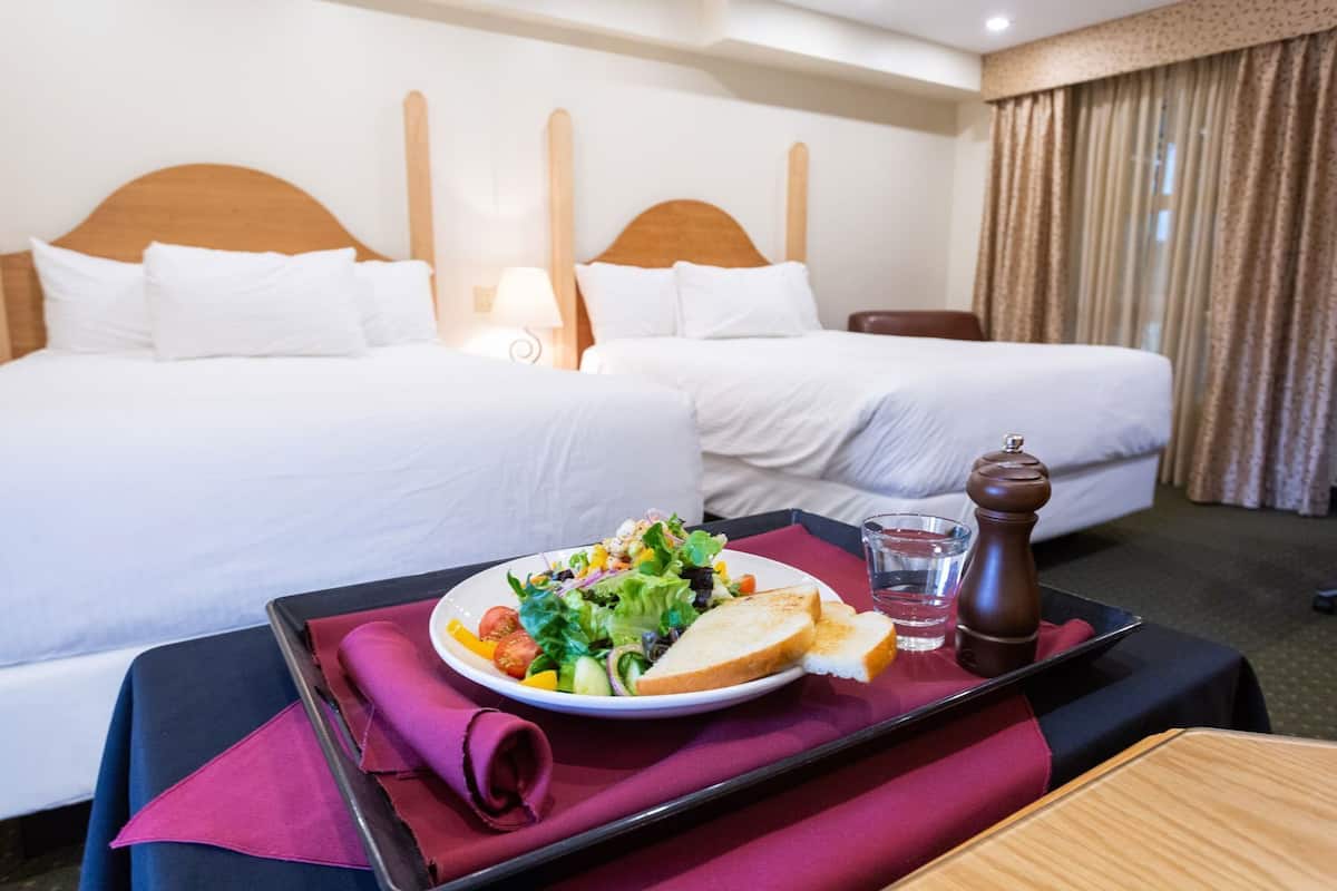 Habitación de hotel con dos camas, una mesa de comedor con un plato de comida, un vaso de agua y un molinillo de pimienta.
