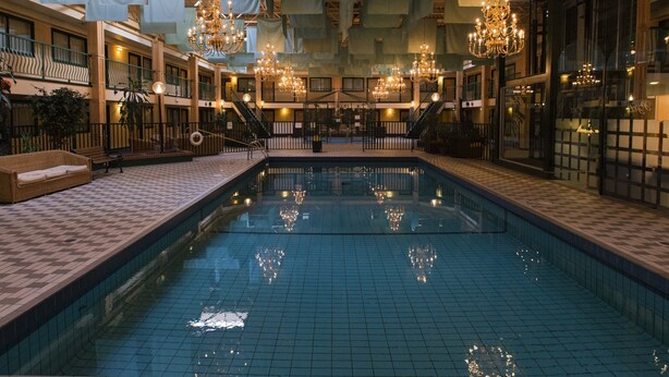 An indoor swimming pool with chandeliers, tiled flooring, and a checkered pattern. - Park Place Lodge (Fernie)