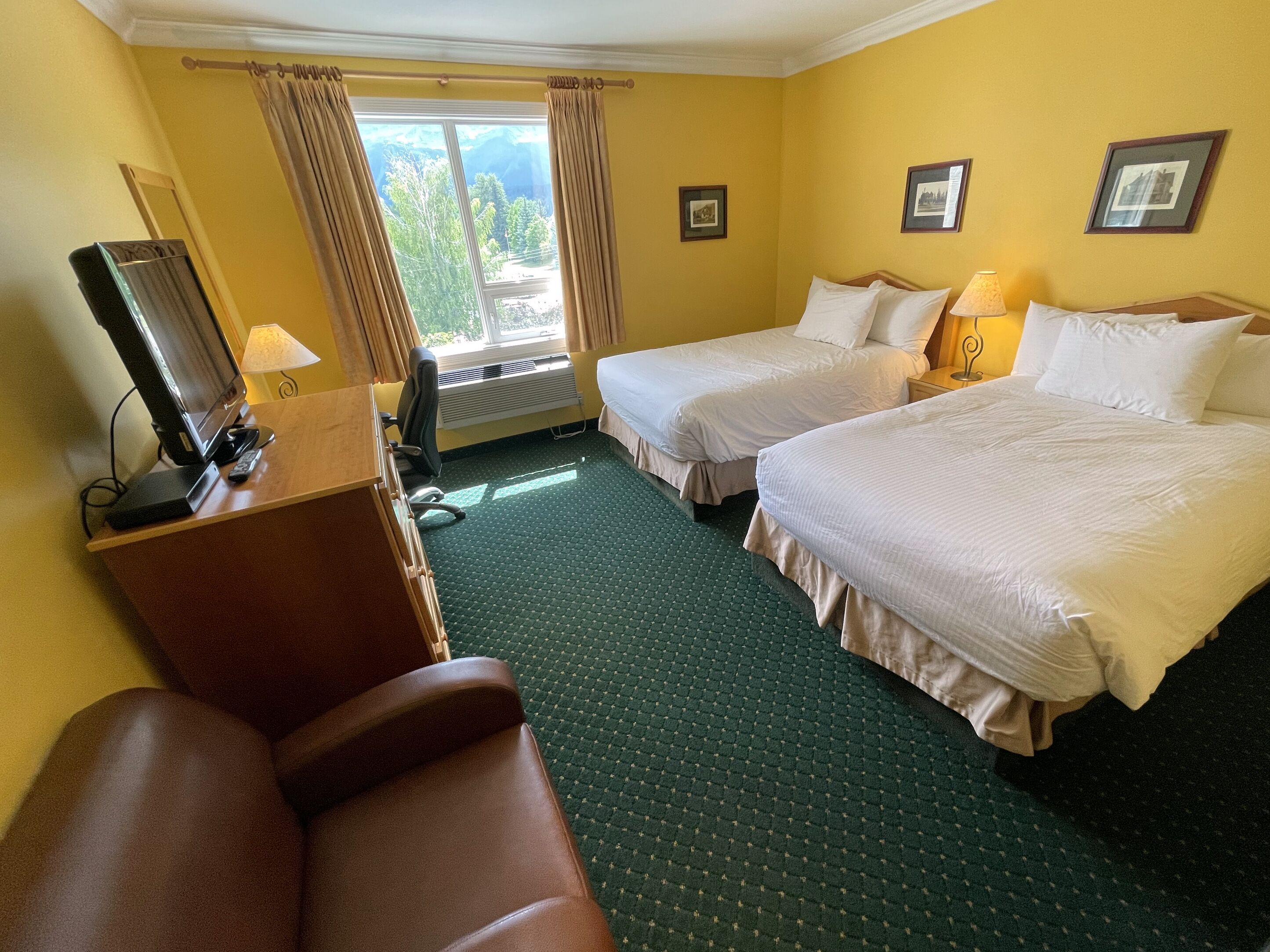 A hotel room with two beds, a desk with a television, and a view of the outdoors.