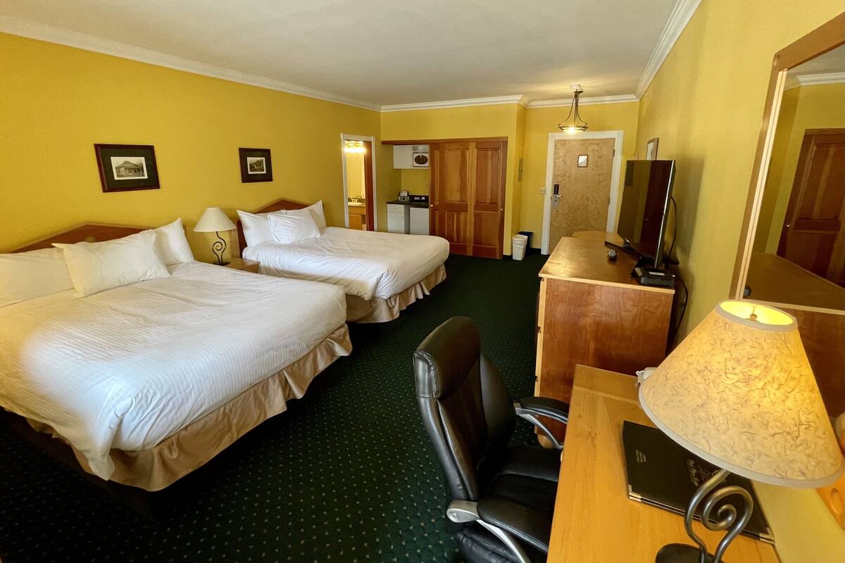 Una habitación de hotel con dos camas, un escritorio con lámpara, una silla, televisor y un espejo.