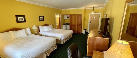 A hotel room with two beds, a desk with a lamp, a chair, a television, and a mirror.
