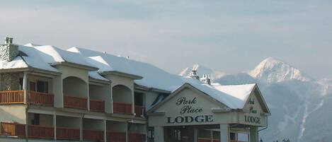 A multi-story building with a sign reading "Park Place Lodge." It features balconies with wooden railings and a snow-covered roof.