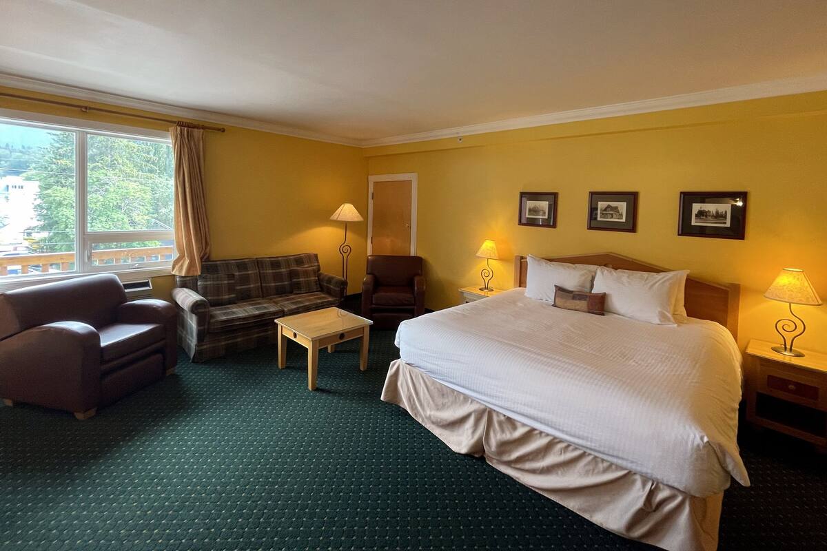 Una habitación de hotel con cama, sofá, sillón, una mesita y una ventana con cortinas.