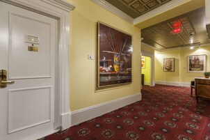 A hallway with a patterned carpet, a large abstract painting on the wall, and a door with a number plate.