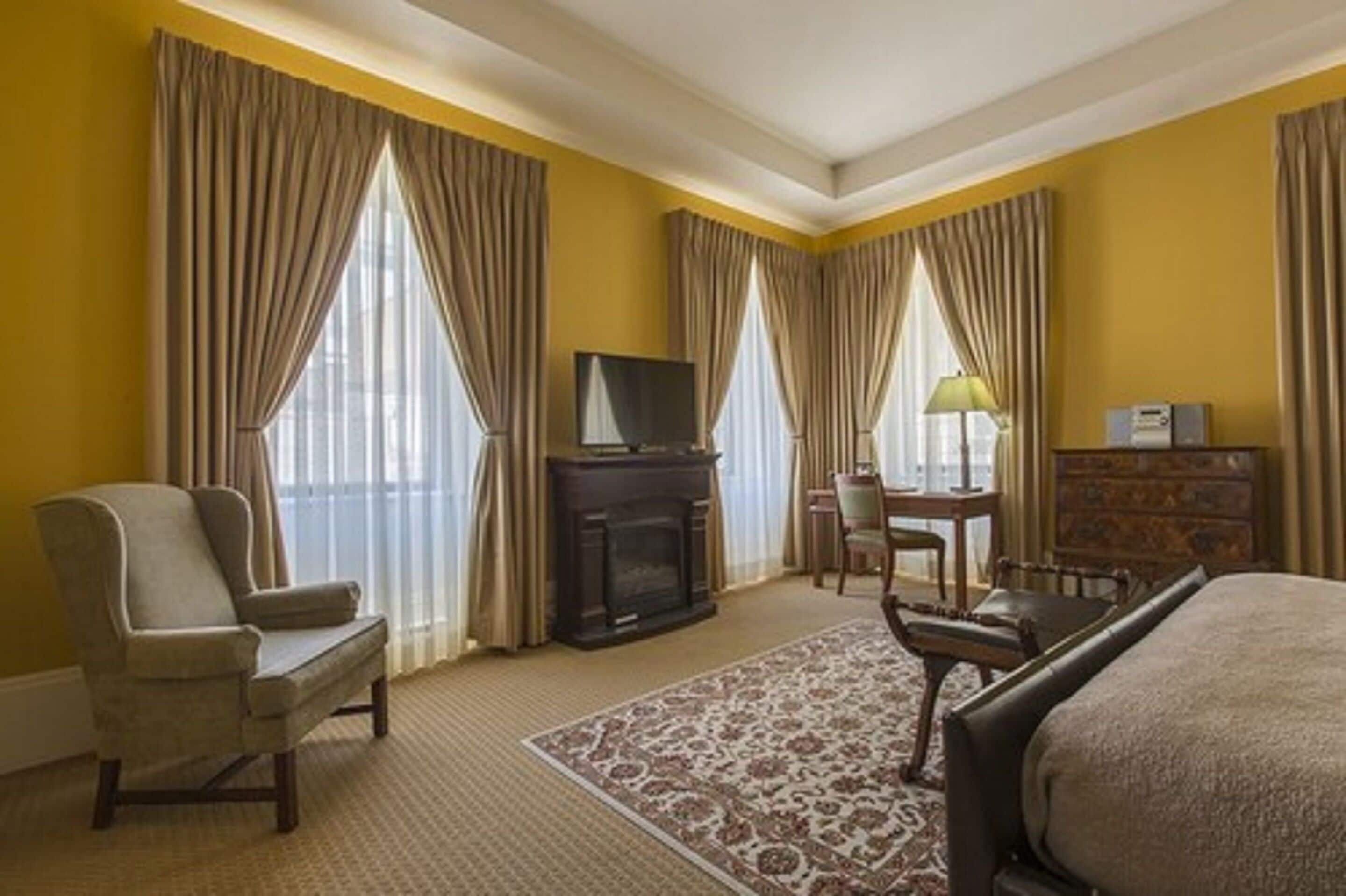 Una habitación de hotel con una cama grande, televisión, chimenea, escritorio y una silla.