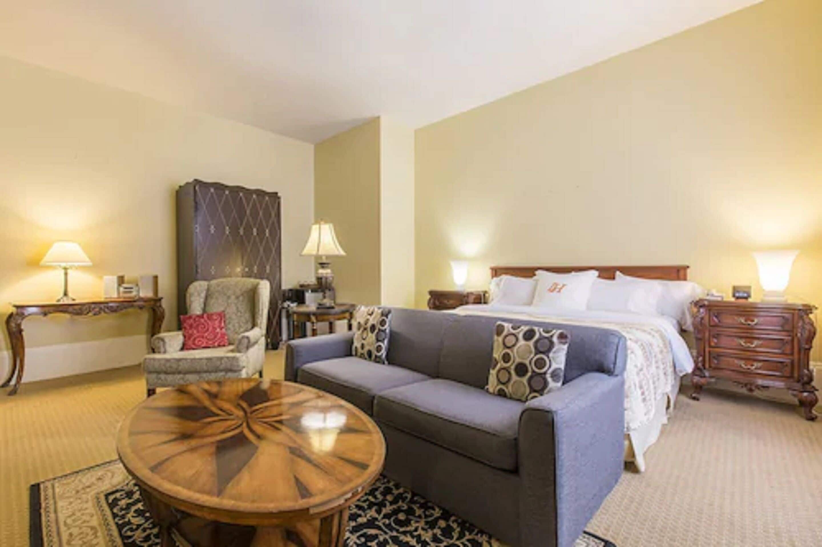 A hotel room with a bed, a sofa, a chair, a round coffee table, and a nightstand.