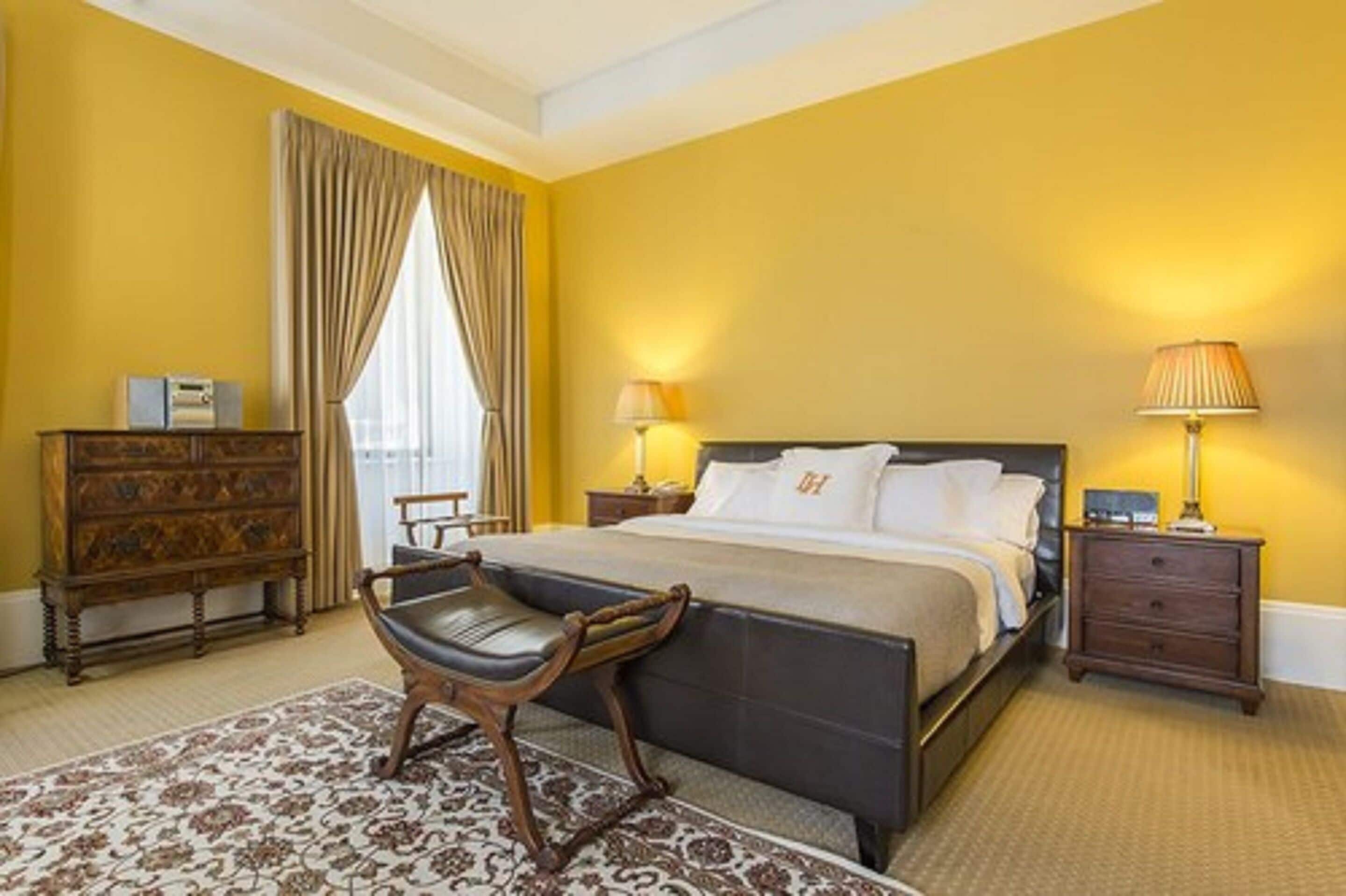 A hotel room with a bed, two bedside tables, a wooden dresser, a chair, and a patterned rug.