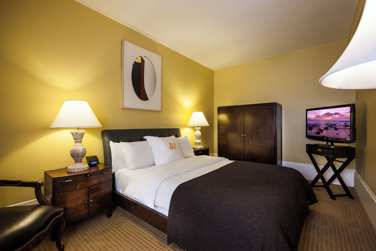 A hotel room with a bed, two bedside lamps, a television, a desk, and a chair.